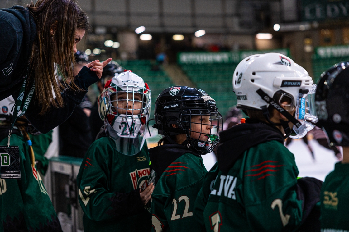 Kids in hockey gear sitting watching a men's hockey game