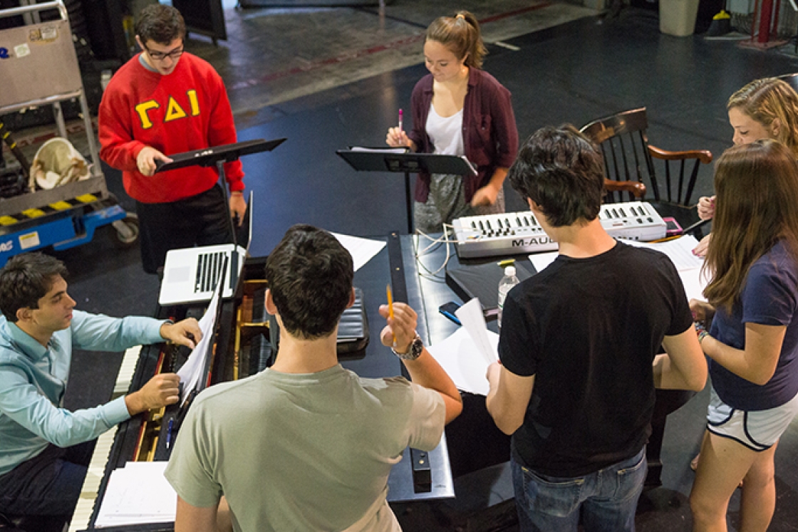 students gathered around a piano rehearsing a play