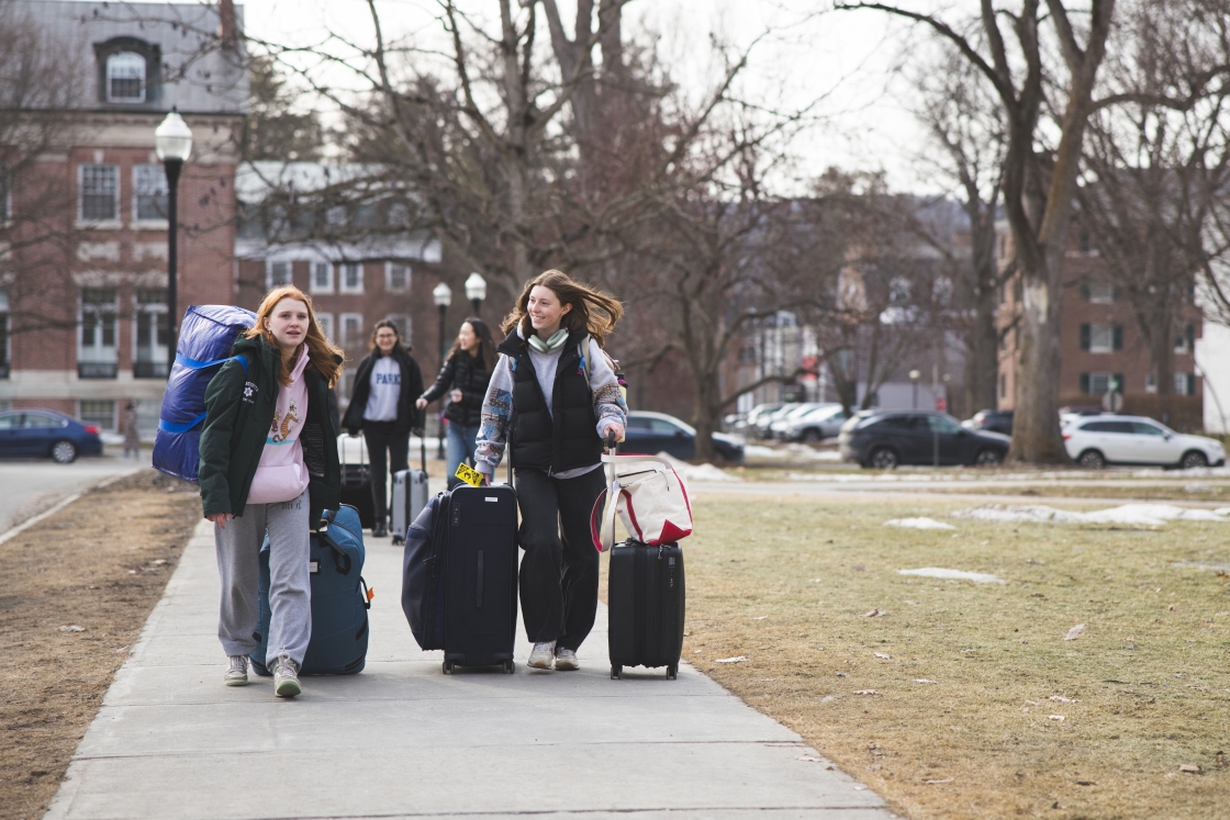Students rolling luggage down the sidewalk