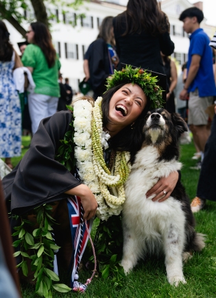 A graduate decked in leis bends down to hug a dog