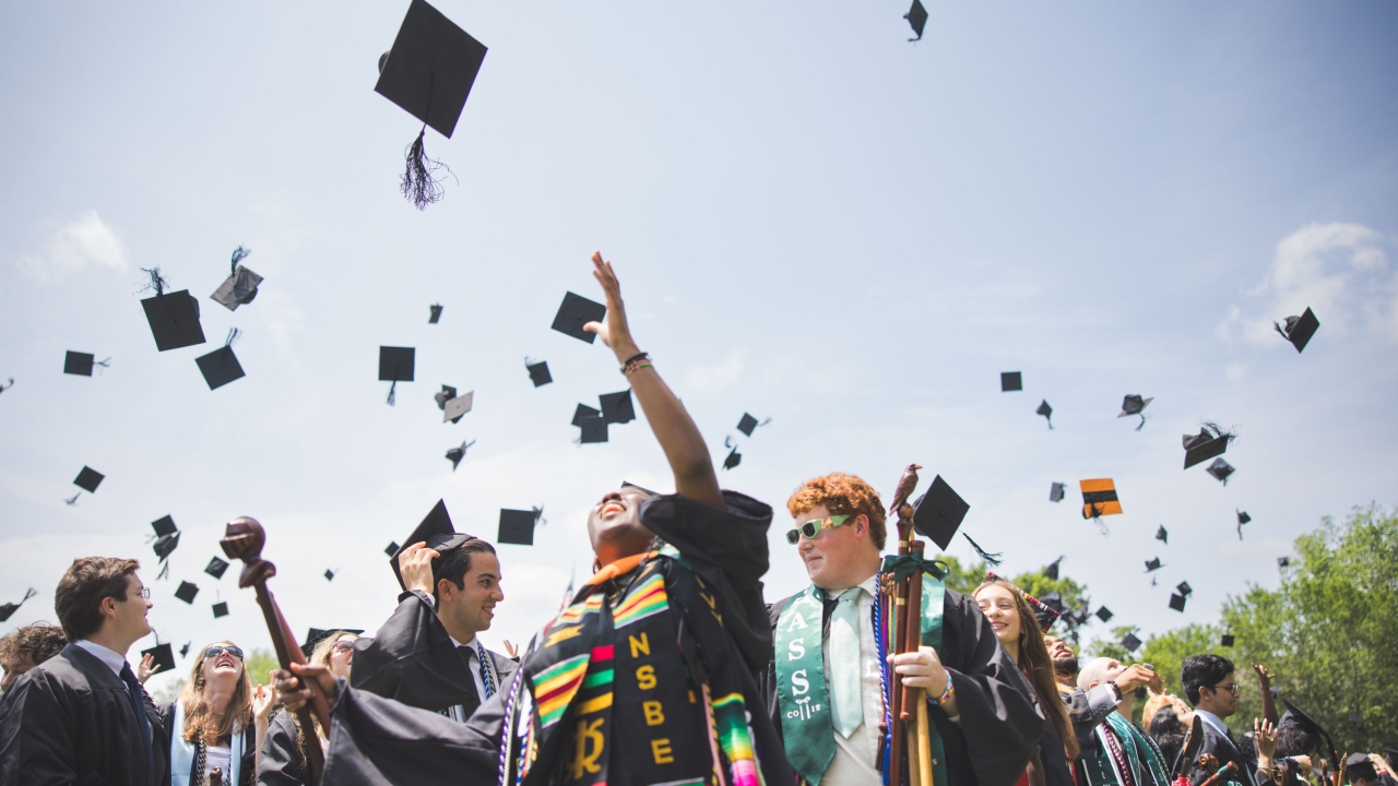 Graduates toss their caps into a sunny and blue sky