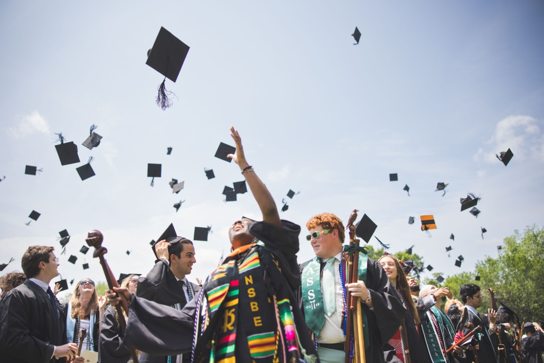 Graduates toss their caps into a sunny and blue sky