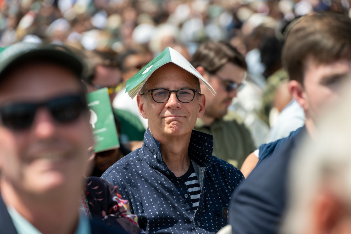 A parent wears a program on their head during the ceremony