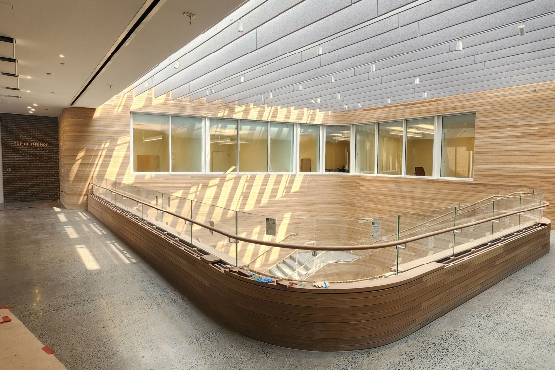Large open space with sunlight, windows, and wood paneling, looking down towards a staircase