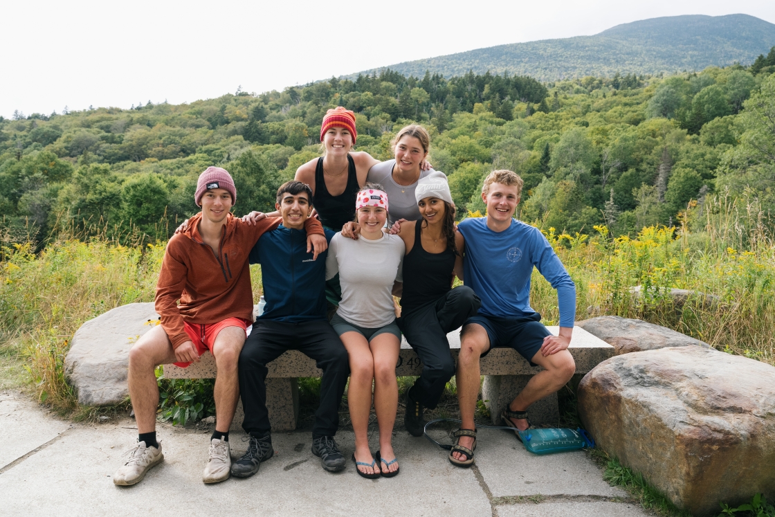 a group of students sits together smiling at the camera in hiking gear