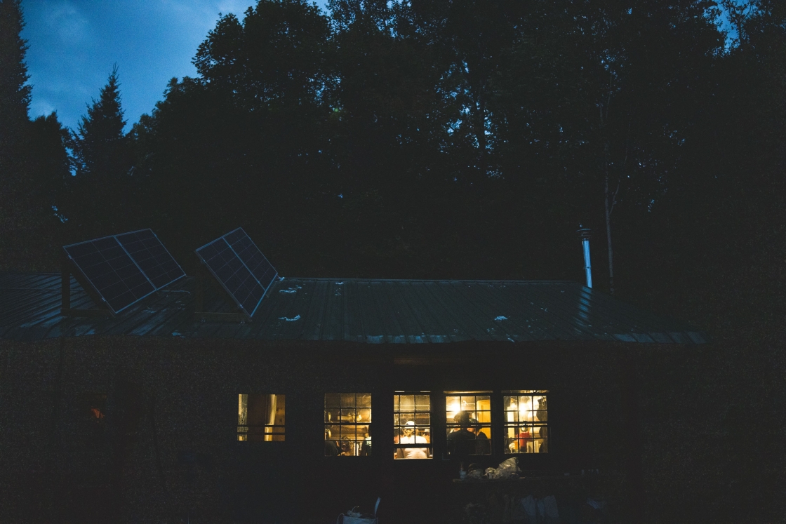 Exterior of a cabin a dusk, with warm lighting shining through the windows