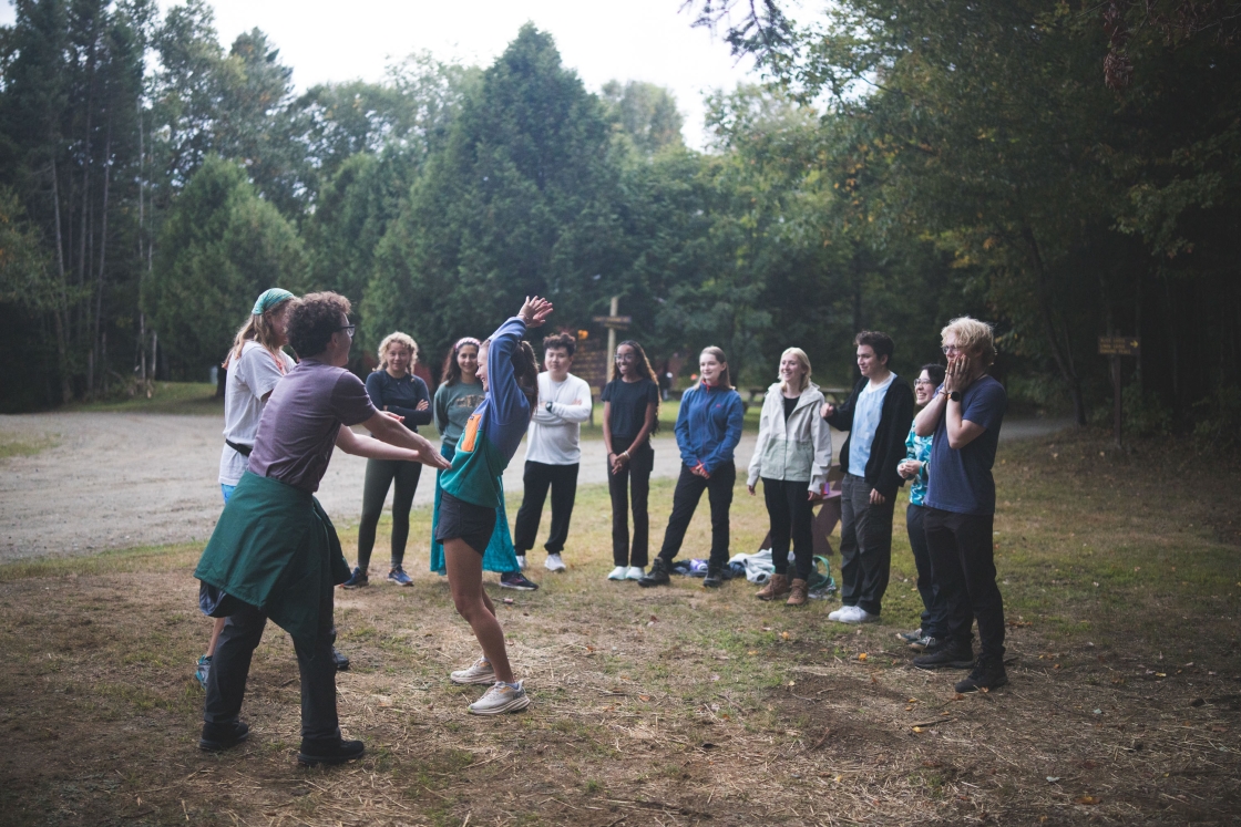 Students stand in a semicircle and watch two people perform lumberjack charades
