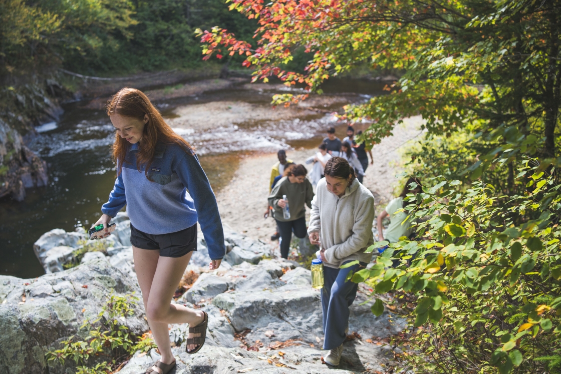 Students hike up rocks from the river bank