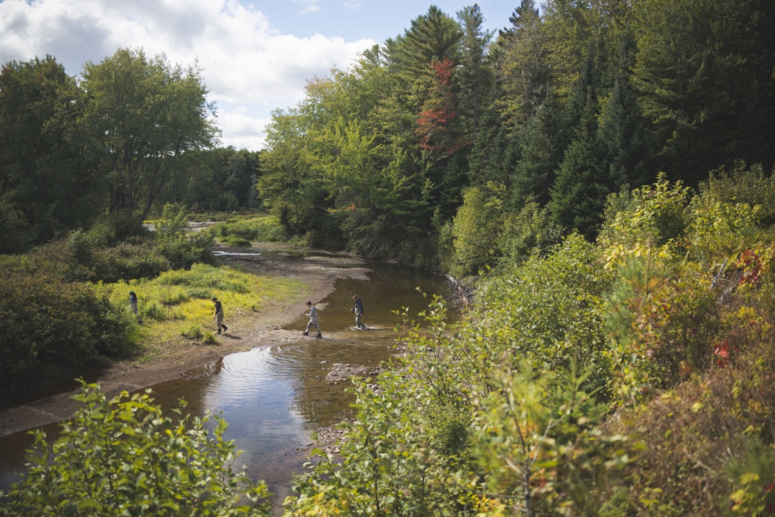 Students in waders with fishing rods exit a spot on the river
