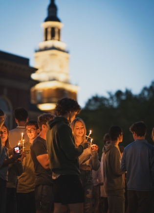 Students light each others candles in front of Baker Berry Library