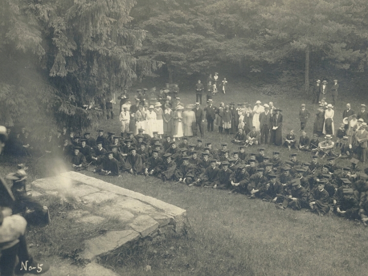Graduates sitting in the grass listening to a speaker