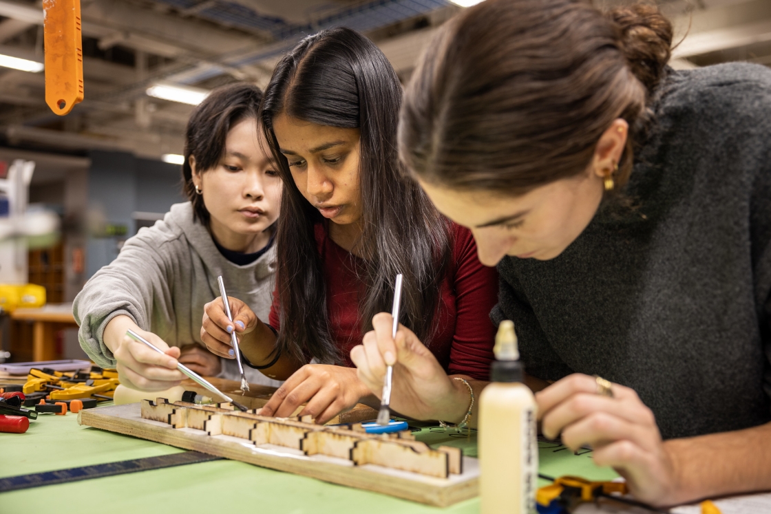 Three students working on a model sitting on a table top.